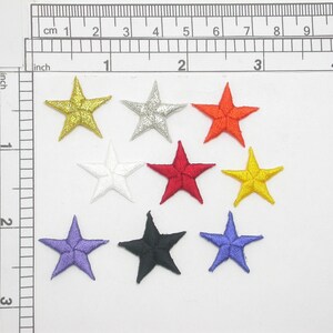 May include: Assortment of eight embroidered iron-on patches in the shape of stars. The stars are in various colors, including gold, silver, red, orange, yellow, white, purple, and black.