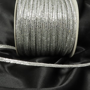 May include: A spool of silver metallic trim with a herringbone pattern. The trim is approximately 1.2 cm wide.