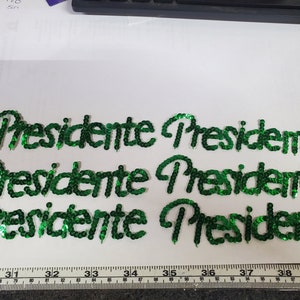 May include: Six green sequined patches spelling out the word "Presidente" in cursive.