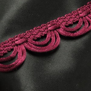 May include: Burgundy red trim with a scalloped edge and fringe detail. The trim is made of a soft, woven fabric and has a delicate, feminine look.