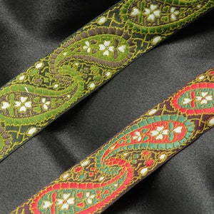 May include: Two paisley patterned trim ribbons, one green and brown, the other red and green, on a black background.