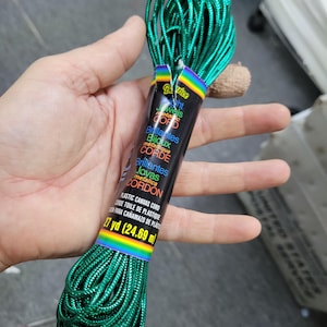May include: A spool of emerald green metallic cord, labeled "ht Jewels Metallic Cord," is held in a hand. The label also includes text in French and Spanish, and indicates 27 yards (24.69 m) of cord.