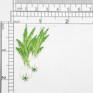 May include: A white and green embroidered patch of a bunch of garlic with green stems.