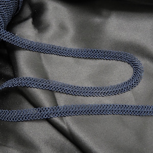 May include: A spool of navy blue trim with a decorative, looped design. The trim is shown on a dark gray fabric background.