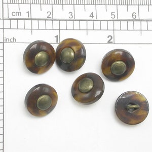 May include: Six oval-shaped buttons with a tortoiseshell pattern and a brass-colored center. The buttons are approximately 0.75 inches in diameter. One button shows the loop on the back for sewing.
