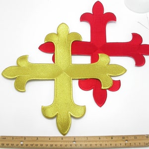May include: Two embroidered crosses, one gold and one red, with a fleur-de-lis design. The crosses are approximately 5 inches in size.