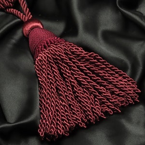 May include: A deep burgundy tassel with a twisted cord, against a black satin background.