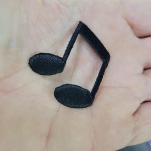 Può includere: Una toppa ricamata nera a forma di croma. Il simbolo musicale è realizzato in tessuto strutturato e presenta due teste di nota arrotondate collegate da un gambo e un'asta. La toppa è progettata per essere cucita o stirata sul tessuto.