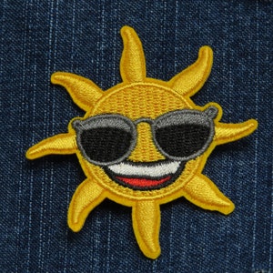 May include: A yellow smiling sun with sunglasses, embroidered on a blue denim background.