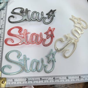 May include: Four plastic "Star" ornaments in different colors: silver with black outline, red with silver outline, blue with silver outline, and white with silver outline.
