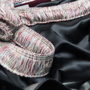 May include: A close-up of a black fabric with a colorful fringe trim. The fringe is made of a variety of colors, including red, white, and blue.