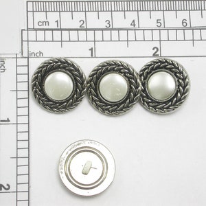 May include: Three silver-toned buttons with a pearl-like center and a braided border. The buttons are approximately 1 inch in diameter. One button has a shank on the back. The buttons are on a white surface.