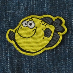 Op de afbeelding: Gele en zwarte geborduurde strijkpatch van een cartoonvis met een glimlachend gezicht.