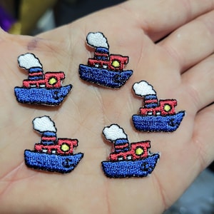 May include: Five embroidered patches of cartoon boats. Each patch features a blue boat with a red cabin and a white smoke stack. The patches are small and detailed, with yellow and black accents.
