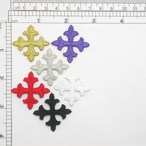 Könnte beinhalten: Sechs gestickte Bügelbilder in Form eines Kreuzes. Die Kreuze sind in Gold, Lila, Silber, Rot, Weiß und Schwarz.