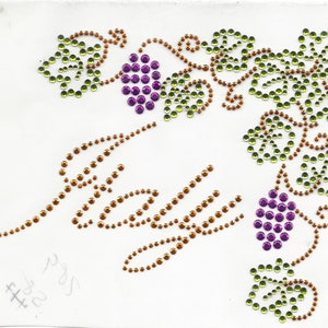 Könnte beinhalten: Das Wort "Italien" ist in braunen Strasssteinen geschrieben, mit einem Weinstockmuster aus grünen und braunen Strasssteinen. Es gibt drei Trauben aus violetten Strasssteinen.