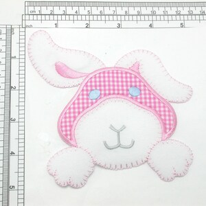 May include: A pink and white felt bunny applique with blue eyes. The bunny is wearing a pink and white gingham hat.