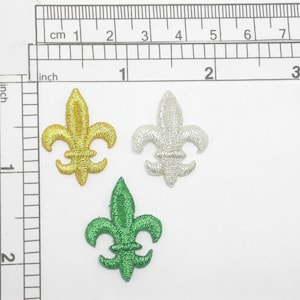 May include: Three embroidered iron-on patches in the shape of a fleur-de-lis. The patches are gold, silver, and green.