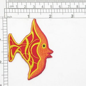 Op de afbeelding: Een geborduurde strijk-op patch van een cartoonvis in rood en geel. De vis heeft een groot, rond lichaam en een kleine staart. De ogen van de vis zijn geel.