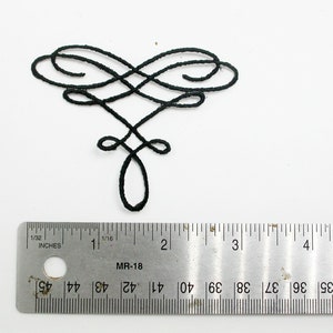 May include: A black decorative flourish design with intricate swirls and loops. The design is approximately 2.5 cm in height.