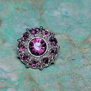 May include: A silver-toned button with a large, round, pink rhinestone surrounded by smaller pink rhinestones.