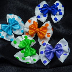 May include: Five white fabric hair bows with polka dots and different colored ribbon centers. The bows are blue, orange, green, purple, and blue.