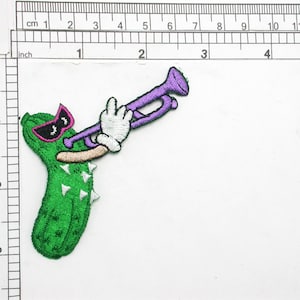 May include: Green pickle cartoon character wearing sunglasses and playing a purple trumpet. The pickle has white spikes and a brown mouth.