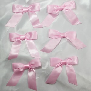 May include: Six pink satin bows with a centre knot. The bows are arranged in two rows of three on a white background.