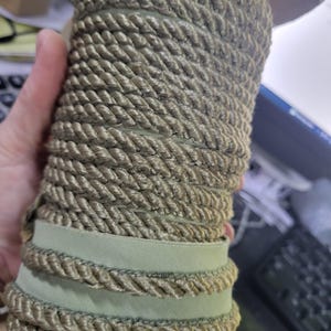 Può includere: Rullo di passamaneria in corda verde oliva con un design a corda ritorta. La passamaneria è avvolta su se stessa, con un accento di nastro verde chiaro. Questa passamaneria decorativa è adatta a vari progetti di artigianato e design.