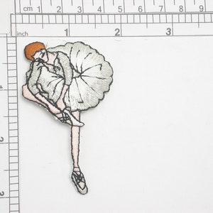 May include: A white embroidered iron-on patch of a ballerina in a white tutu with a pink bodice and red hair. The ballerina is in a pose with one leg extended and the other leg bent at the knee.
