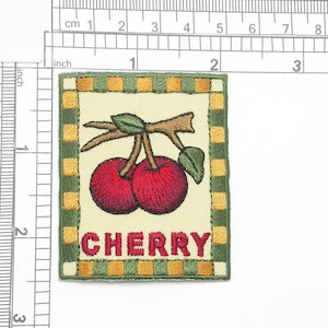 May include: Embroidered patch with a green border and yellow squares. The center features a white background with two red cherries on a brown branch. The text "CHERRY" is embroidered in red below the cherries.
