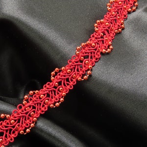 以下が含まれることがあります： 繊細で複雑なデザインの赤いビーズトリム。トリムは薄くて柔軟な素材で作られており、小さな丸いビーズが特徴です。