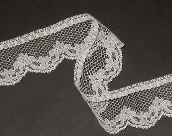 May include: White lace trim with a scalloped edge and a delicate floral pattern. The lace is made of a fine mesh fabric and is perfect for adding a touch of elegance to any project.