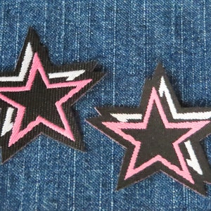 May include: Two black fabric star-shaped patches with pink and white outlines on a blue denim background.