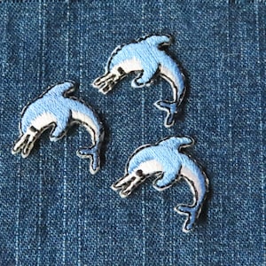 May include: Three blue embroidered dolphin patches on a denim background.