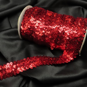 May include: A spool of red sequin trim. The trim is made of small, round sequins that are sewn together in a continuous line. The trim is perfect for adding a touch of sparkle to any project.