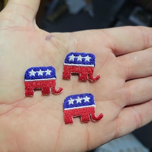 May include: Three embroidered patches in the shape of elephants, each featuring a red body, a blue head with three white stars, and a curled trunk. The patches are small and detailed, with visible stitching.