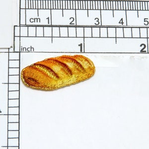 May include: A small embroidered patch of a golden brown loaf of bread, measuring approximately 2.5 cm in length.