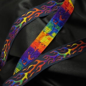 May include: Black ribbon with a flame design in rainbow colors. The ribbon has a dark blue background with flames in shades of red, orange, yellow, green, blue, and purple. The ribbon is on a black background.