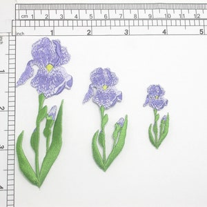 May include: Three purple embroidered iron-on patches of iris flowers with green stems and leaves. The largest patch is about 4 inches tall, the middle patch is about 2.5 inches tall, and the smallest patch is about 1.5 inches tall.