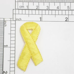 Pode incluir: Uma fita de cetim amarela amarrada em um laço. A fita tem aproximadamente 5 cm de comprimento.