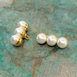 May include: Two sets of gold-toned pearl embellishments. Each set features three round, white pearls.