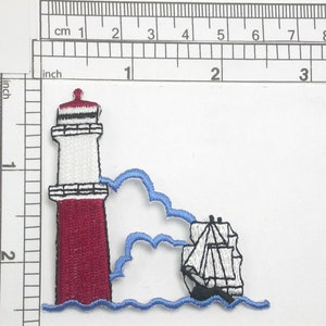 May include: An embroidered patch featuring a red and white lighthouse with a blue wave and a white sailboat in the background.