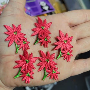 May include: Embroidered red poinsettia flower patches with green stems and centers. These floral appliques are ideal for adding a festive touch to clothing, accessories, or craft projects. Each patch features detailed stitching.