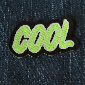 May include: A green and white embroidered patch with the word "cool" in a cursive font. The patch has a black border.