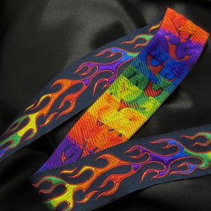 May include: A rainbow colored guitar strap with a flame design. The strap is made of a woven fabric and has a black background.