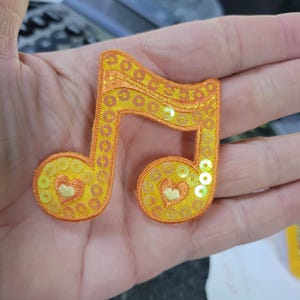 Parche de nota musical con lentejuelas naranjas. Medidas: 2 3/8" de ancho x 2 1/4"