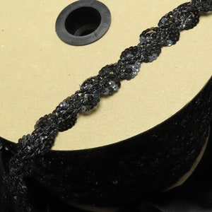 May include: A spool of black sequined trim with a scalloped edge. The trim is wound around a cardboard spool.