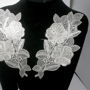 May include: Two white floral lace appliques with delicate embroidery and a sheer fabric. The appliques are perfect for adding a touch of elegance to clothing, accessories, or home decor projects.