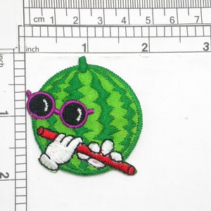 May include: Green watermelon with a purple and black sunglasses and a red straw in its mouth. The watermelon is embroidered with white stitching.